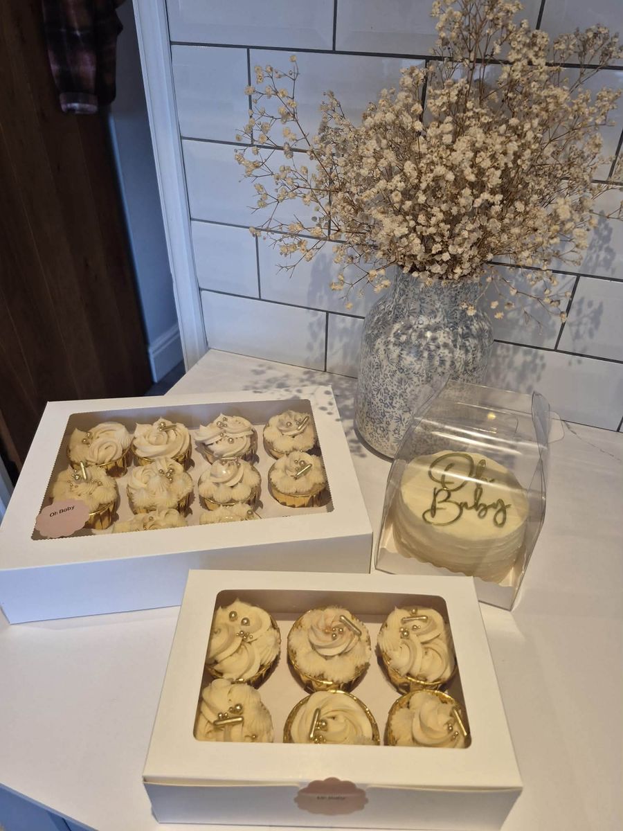 Boxes of cream and gold Oh Baby cupcakes with a small cake