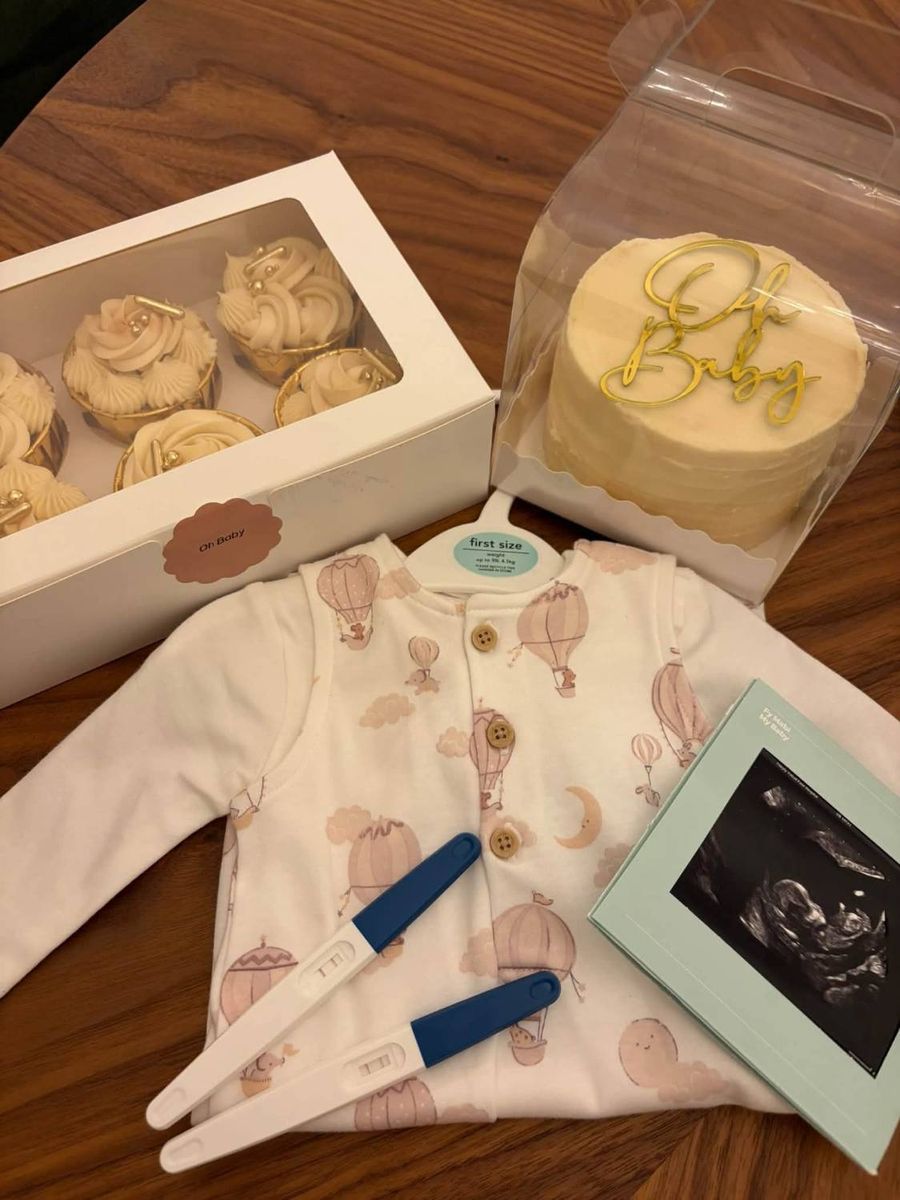 Pregnancy tests, a hot-air-balloon babygrow, scan photo, cupcakes and cake