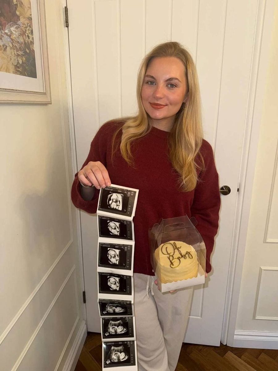 Lucy holding a strip of baby scan photos and an Oh Baby cake